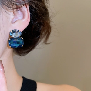 Macro shot of a model wearing gold claw-set blue oval and rectangular gemstone earrings