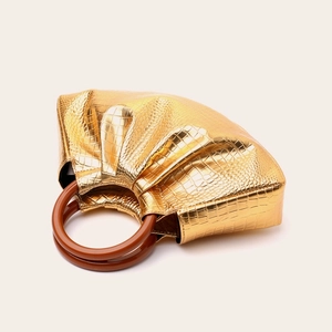 Macro shot of gold crocodile texture handbag with round wooden handle and pleated design