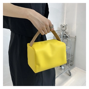 Detail view of a yellow PU leather cube handbag held by a model in a minimalist setting