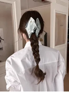 Détail d'une pince à cheveux en satin vert clair avec nœud élégant sur une tresse douce