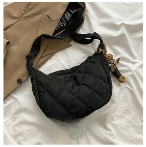 Detail of black quilted nylon bag with plush bear charm on white fabric background