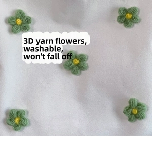 Detail of 3D knitted green yarn flowers with yellow centers on white canvas fabric