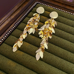 Close-up of golden leaf sequin tassel earrings on dark green velvet display tray