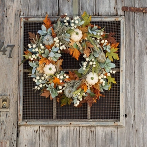 Autumn wreath with pumpkins and maple leaves hanging on a rustic wooden door