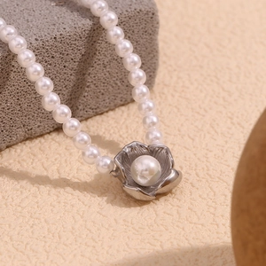 Macro detail of a 18K gold plated flower pendant with central pearl on a pearl chain
