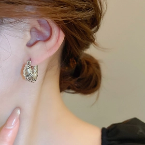 Close-up of a silver U-shaped twisted metal hoop earring worn by a female model