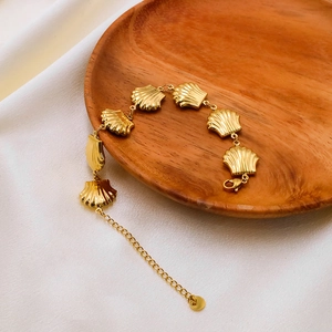 Detail of a golden shell charm bracelet on a wooden stand with white silk backdrop