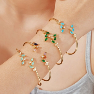 Detailed view of leaf-shaped gold bracelets with colorful turquoise and emerald gemstones