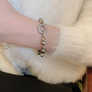 Detailansicht eines grauen Perlenarmbands mit zirkonbesetztem Silberring am Handgelenk