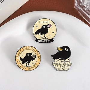 Three-piece black crow enamel pin set with gold and pink gems in a white ceramic dish