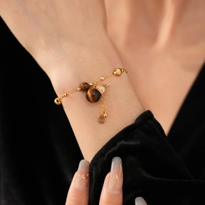 Detail eines Tigerauge-Armbands mit Goldkette und Münzanhänger am Handgelenk getragen