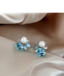 Macro view of silver square zircon pearl earrings on champagne satin fabric background