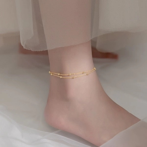 Elegant gold-tone double-layer anklet with bead charms on a model ankle against white silk