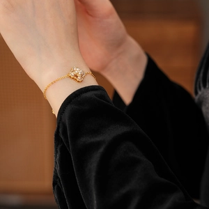 Détail d'un bracelet trèfle doré avec perles et petits diamants sur le poignet d'un modèle
