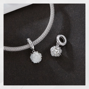 Macro shot of white rose charm on silver braided mesh bracelet against black background