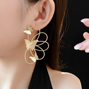 Close-up of elegant gold hollow butterfly drop earrings worn by a model on dark background