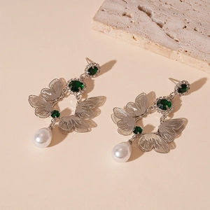 Detail of silver butterfly earring featuring green crystals and white teardrop pearls