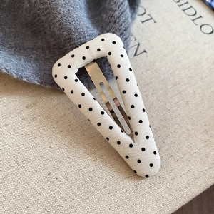 Dettaglio di un fermaglio per capelli a triangolo con pois neri su tessuto di cotone bianco