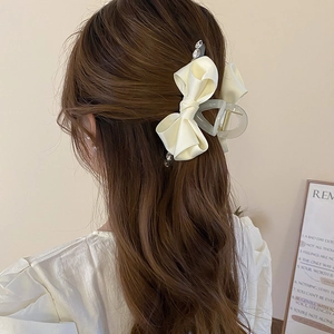 Detail of cream-colored satin bow hair claw clip with rhinestones on model back view