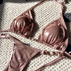 Detail of rose gold metallic bikini with large pearl accents and gold ring hardware