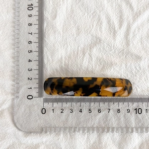 Détail montrant la barrette en acétate écaille de 9 cm sur un tissu en lin blanc épuré
