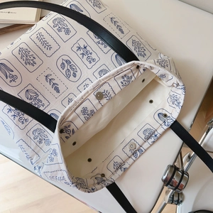 Minimalist off-white canvas tote bag with blue floral print and black leather straps