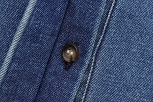 Detailed close-up of dark denim fabric with vintage marble button and reinforced stitching