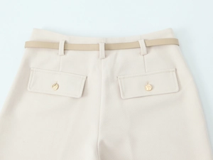 Dettaglio dei pantaloni beige con tasche a patta, bottoni dorati e cintura sottile abbinata