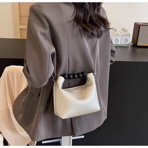 Litchi pattern beige dumpling bag with black bead handle and silver chain on model