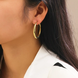 Close-up of model wearing gold hollow hoop earrings with textured rhombic pattern