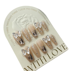 Press-on nails in nude gradient with glitter accents and 3D rhinestone butterfly