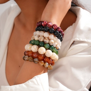 Detail of stacked acrylic beaded bracelets in earthy tones on a model's wrist