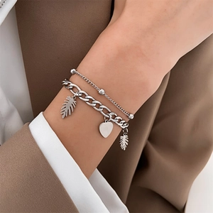 Close-up of double-layer silver chain bracelet with heart and leaf charms on wrist