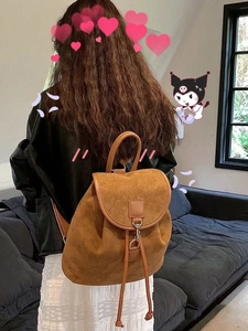 Detail view of a brown suede backpack with drawstring closure and flap cover on shoulder
