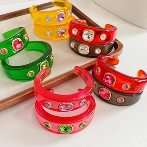 Close-up of colorful resin cuff bracelets with embedded rhinestones on a wooden tray