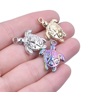 Detailed macro view of 18k gold and silver turtle charms held by hand