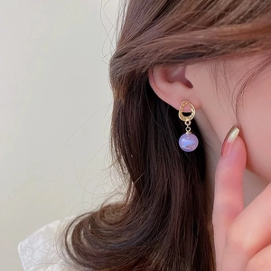 Close-up of a model wearing a gold hoop earring with a purple iridescent pearl detail