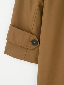 Close-up detail of the brown trench coat cuff with a black button on twill fabric