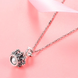 Macro shot of a silver crown pendant with white pearl on a necklace with pink ribbon