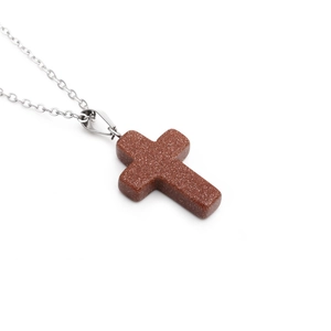 Close-up of brown goldstone cross pendant on polished stainless steel chain