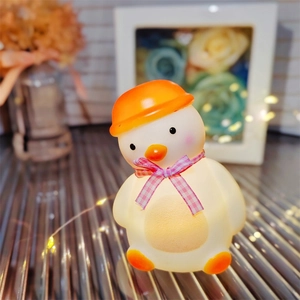 Detail of yellow duck night light with orange hat and pink ribbon glowing softly