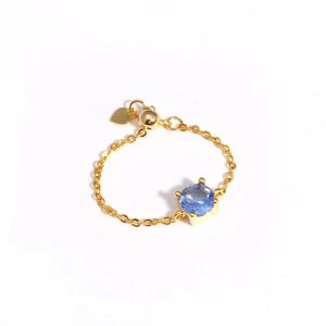 Detail of adjustable gold chain ring featuring a blue gemstone and tiny heart pendant