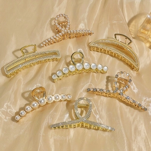 Elegant gold metal hair claw clips with pearls and rhinestones on silk background