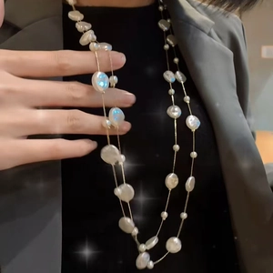 Detailed view of elegant long layered pearl necklace with golden chain on dark attire