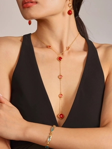 Dettaglio della collana dorata con nappe e pietre rosse quadrate su un abito da sera nero
