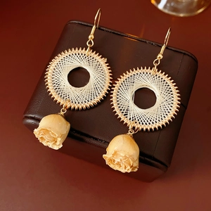 Close-up of woven gold hoop earrings with beige preserved roses on leather case