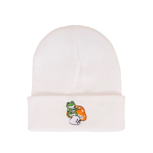 Close-up of white ribbed knit beanie featuring green frog and mushroom embroidery