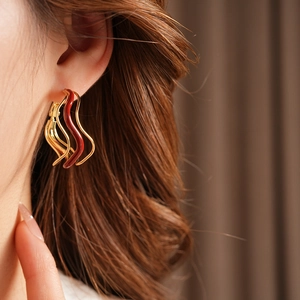 Close-up of wavy gold earrings with dark red enamel dripping on a model's ear