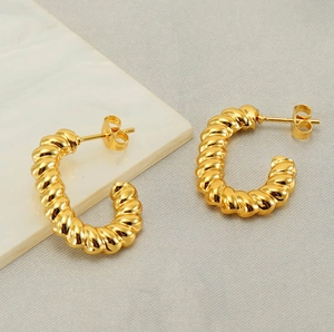 Detail shot of golden spiral twist hoop earrings on white marble and grey fabric background