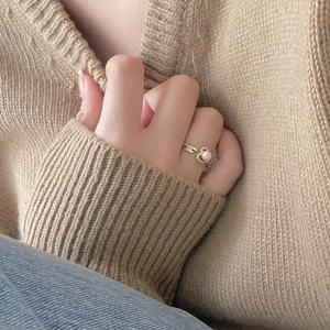 Detailed view of a gold heart pearl ring with woven texture on a beige knit background